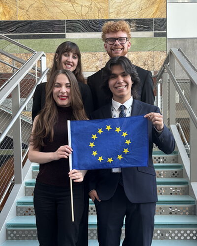 Students who participated in Midwest Model European Union in 2026 pose for a picture on the steps holding a small EU flag.